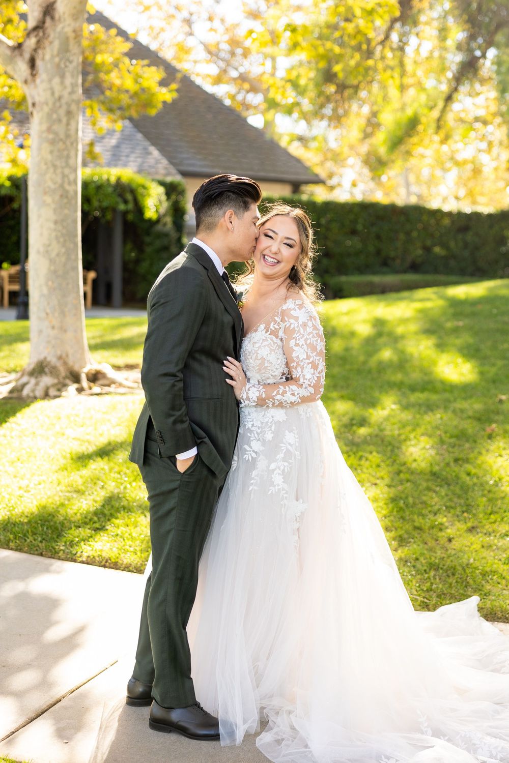 Happy newlyweds share romantic moments in a sunlit garden setting with trees during an autumn wedding celebration.