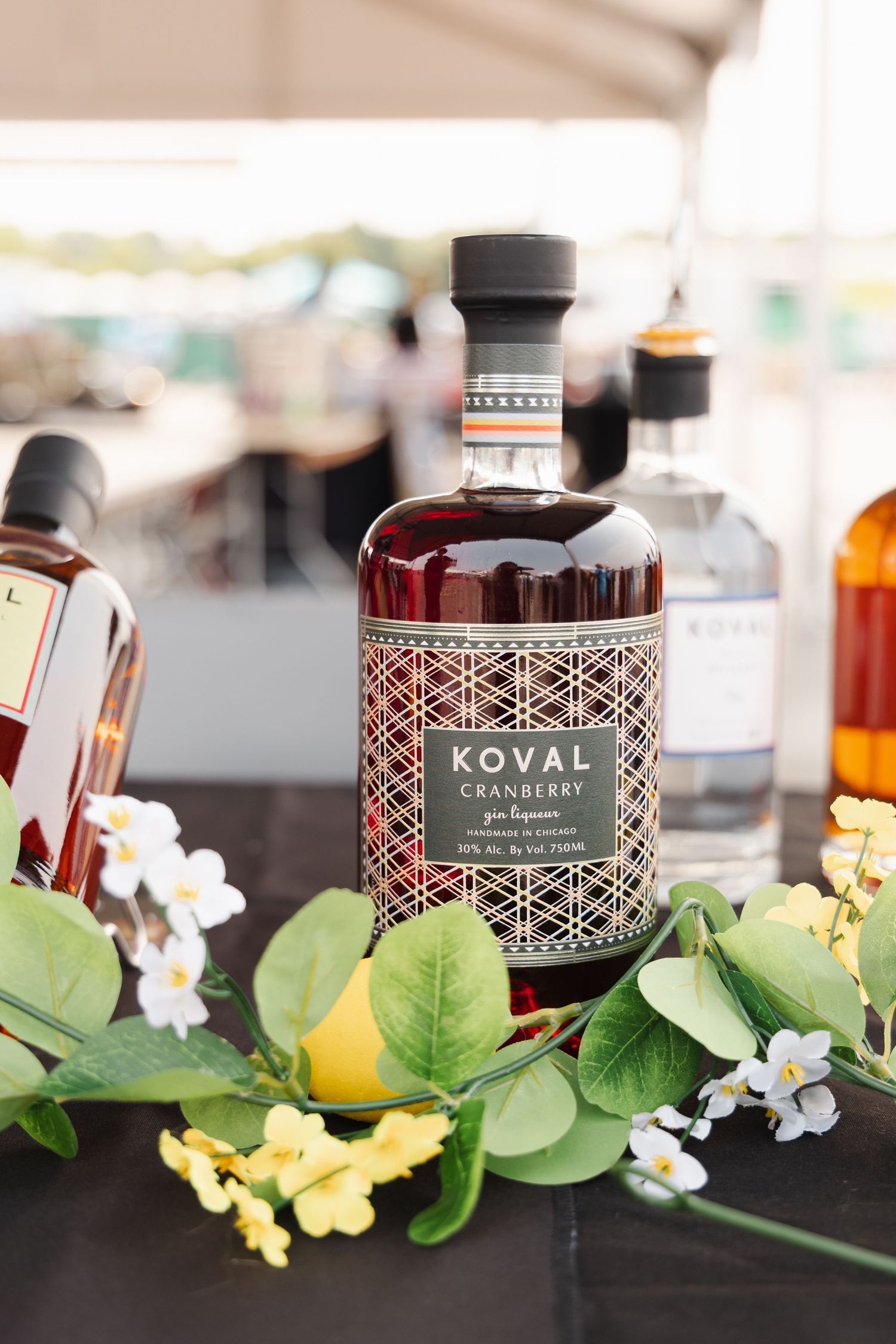 Koval liquor bottles on display with decorative greenery and yellow flowers.