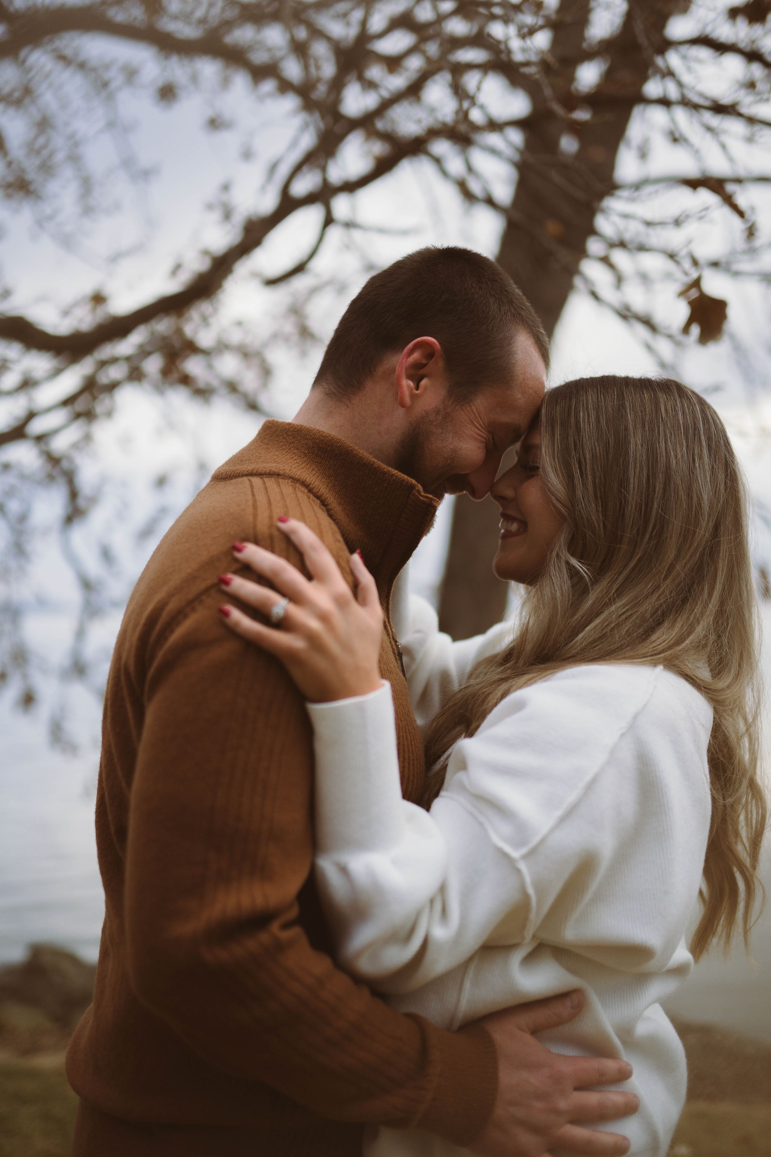 Romantic couple in brown and white sweaters embracing under autumn trees.