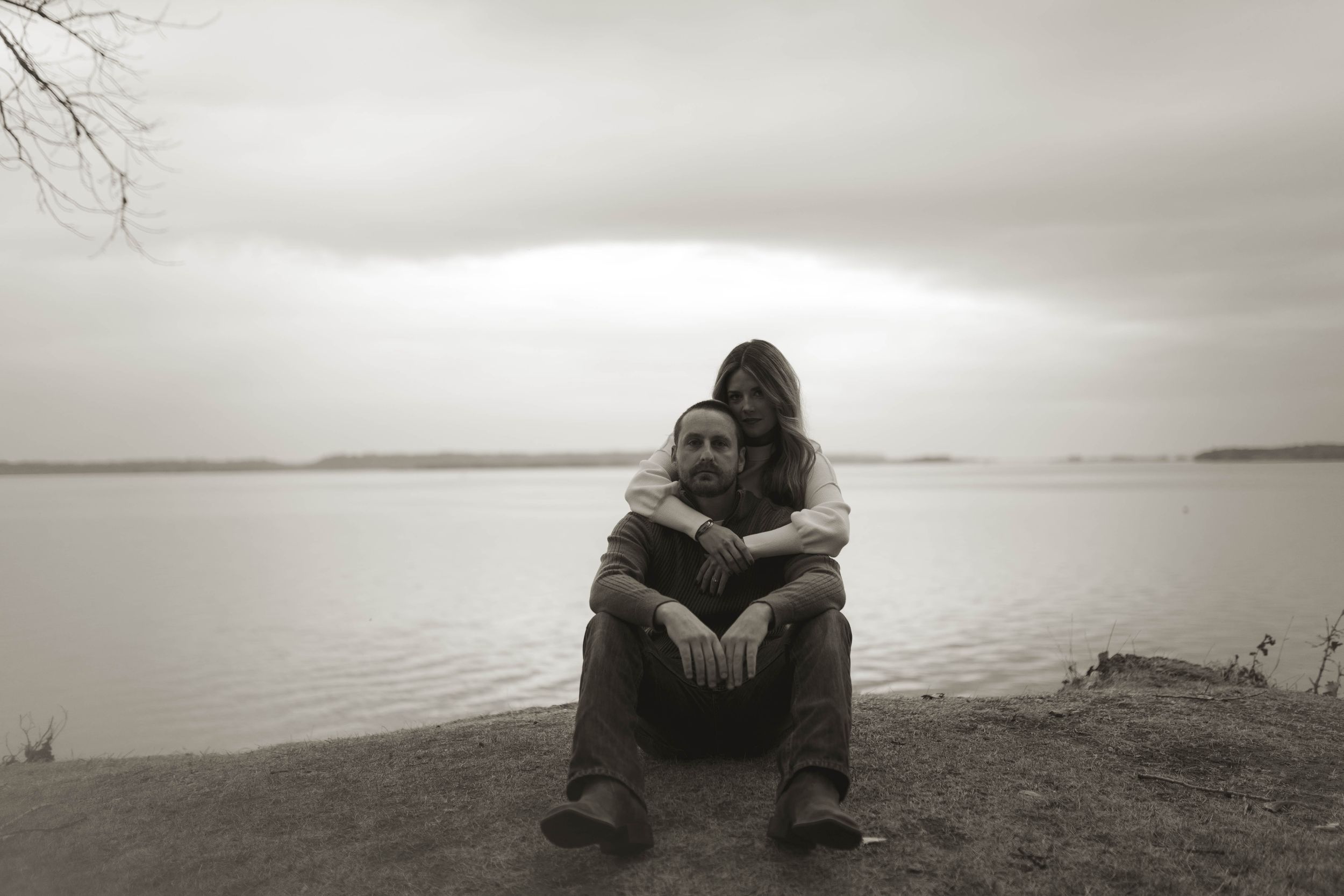 Couple sits together on a cliff overlooking a serene waterfront view.
