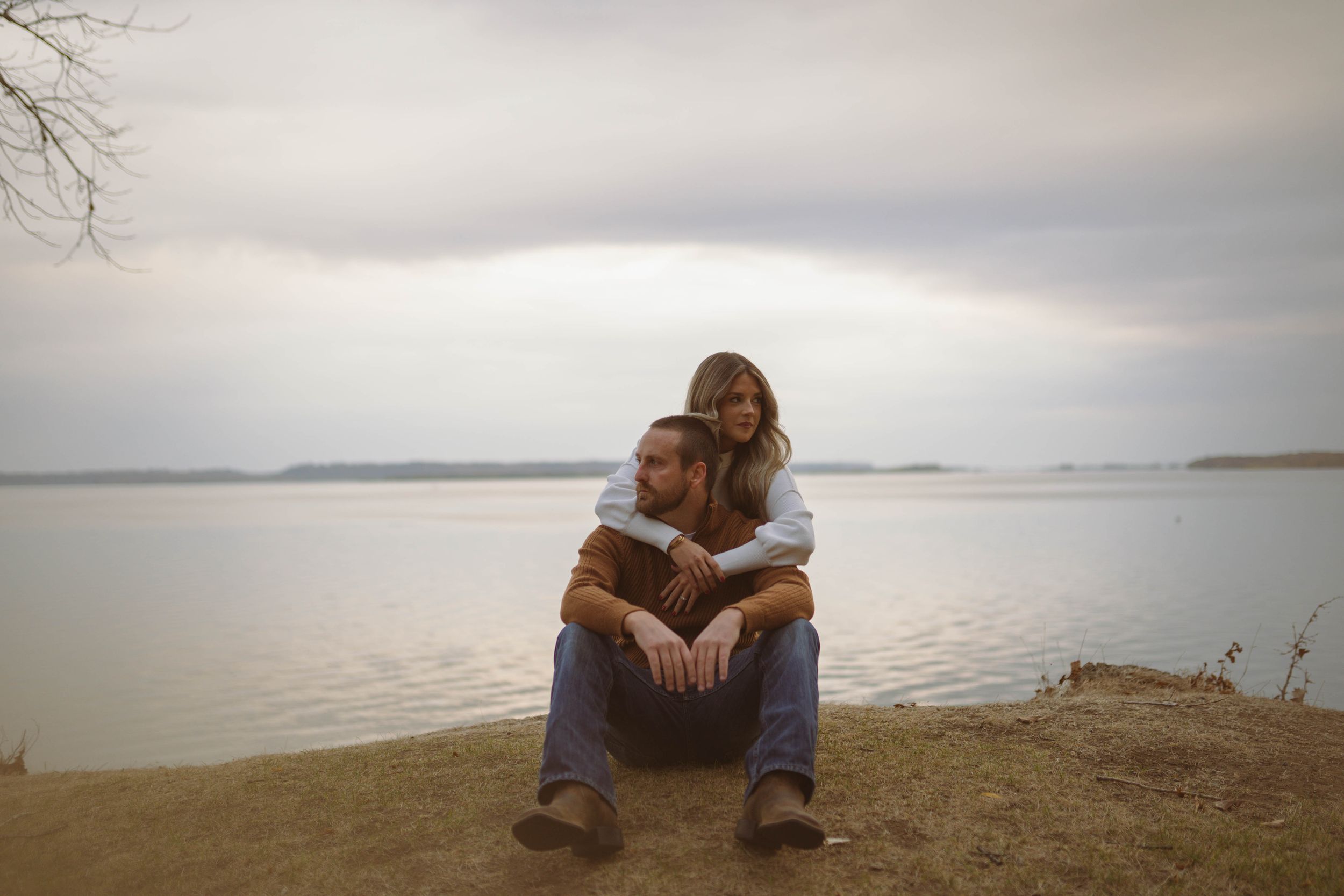 Two people share an intimate moment by the water on an overcast day.