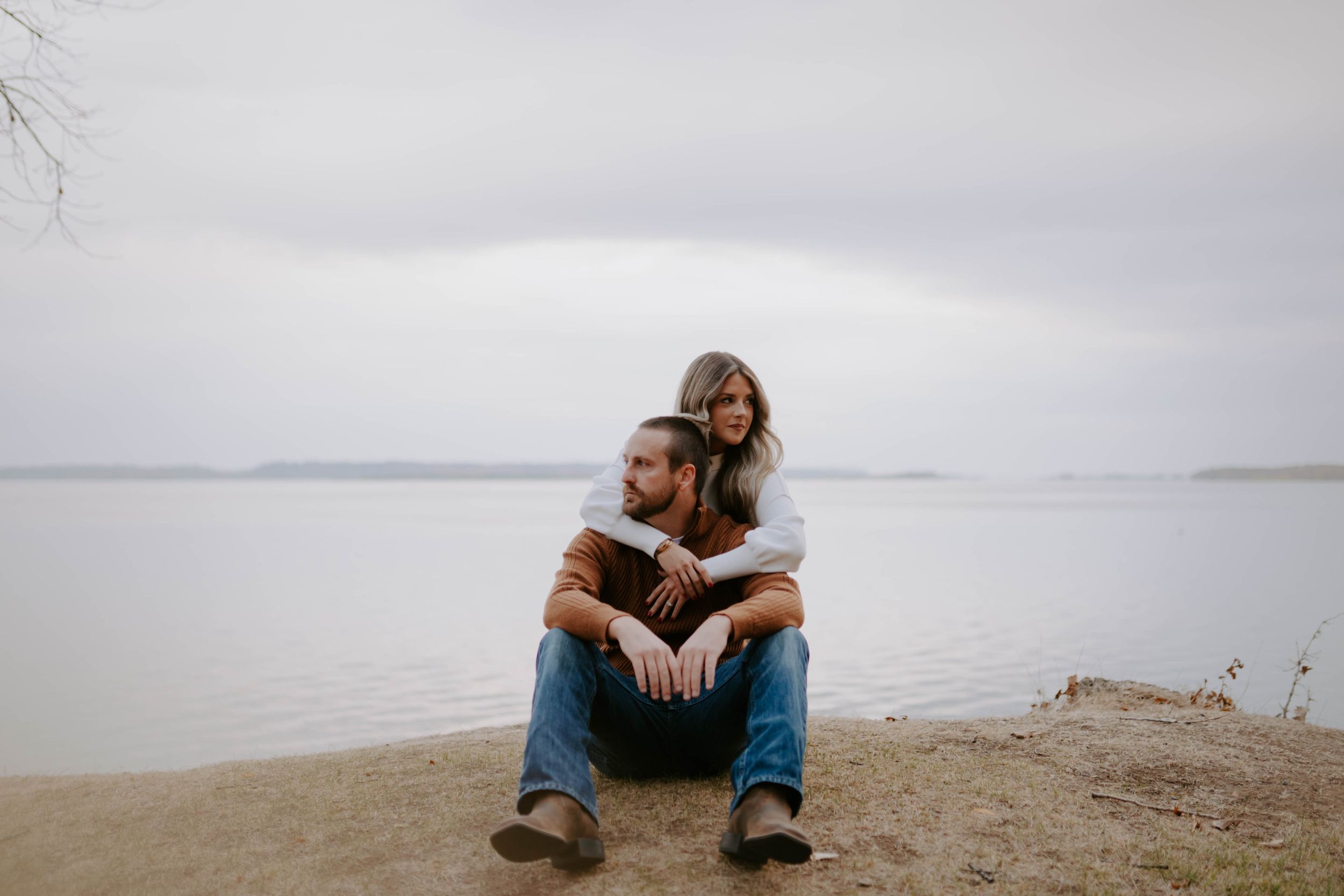 Couple sitting together on shoreline overlooking calm waters.