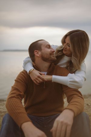 Playful couple laughs and embraces on a cloudy day by the water.