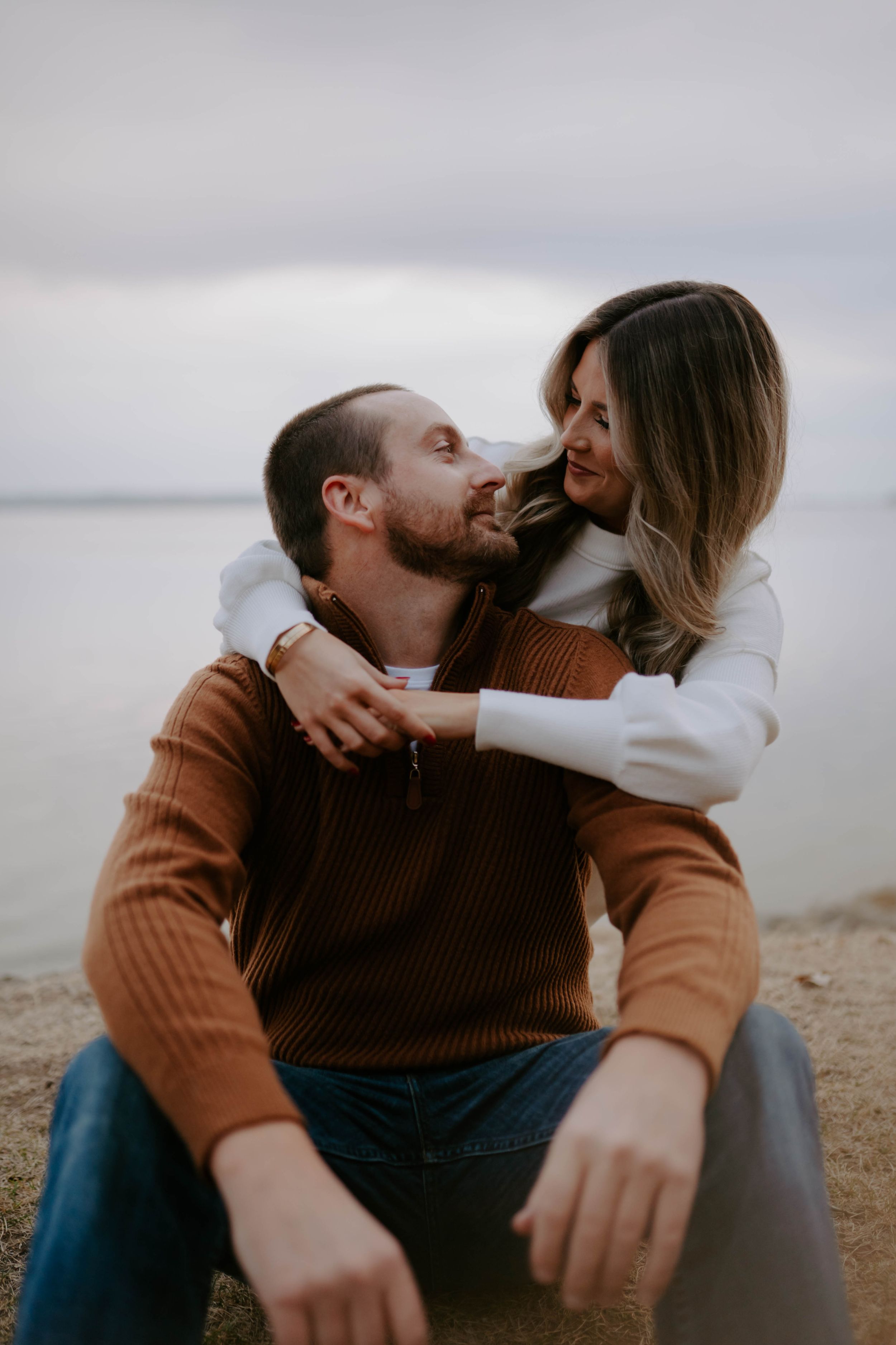 Romantic couple embraces while sitting together on a coastal cliff.