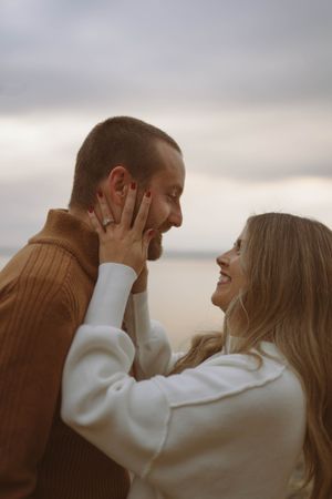 Couple embraces tenderly against cloudy coastal backdrop.