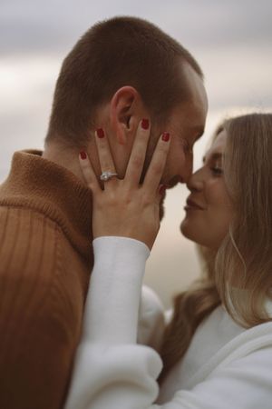 Close-up of couple embracing with woman's red-painted nails visible on partner's face.