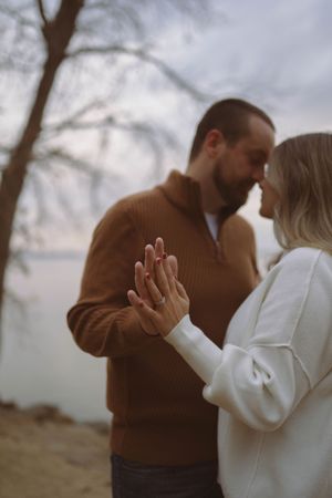 Couple in brown and white sweaters embracing outdoors with trees in background.
