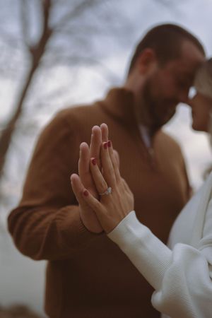 Artistic shot focusing on hands and embrace of couple in coordinated winter outfits.