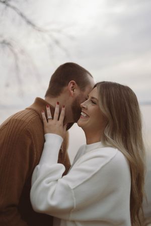 Joyful couple laughing and embracing in white and brown sweaters outdoors.