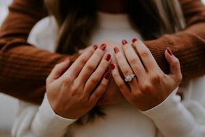 Close-up shot of hands with red nail polish and an engagement ring.