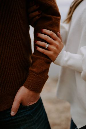Close-up of hands and engagement ring with brown sweater and white top in frame.