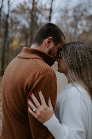 A couple in autumn attire embraces tenderly in a wooded setting during a romantic photoshoot.
