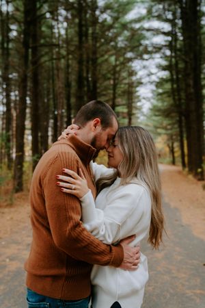 A romantic couple in casual fall clothing shares intimate moments along a tree-lined path.