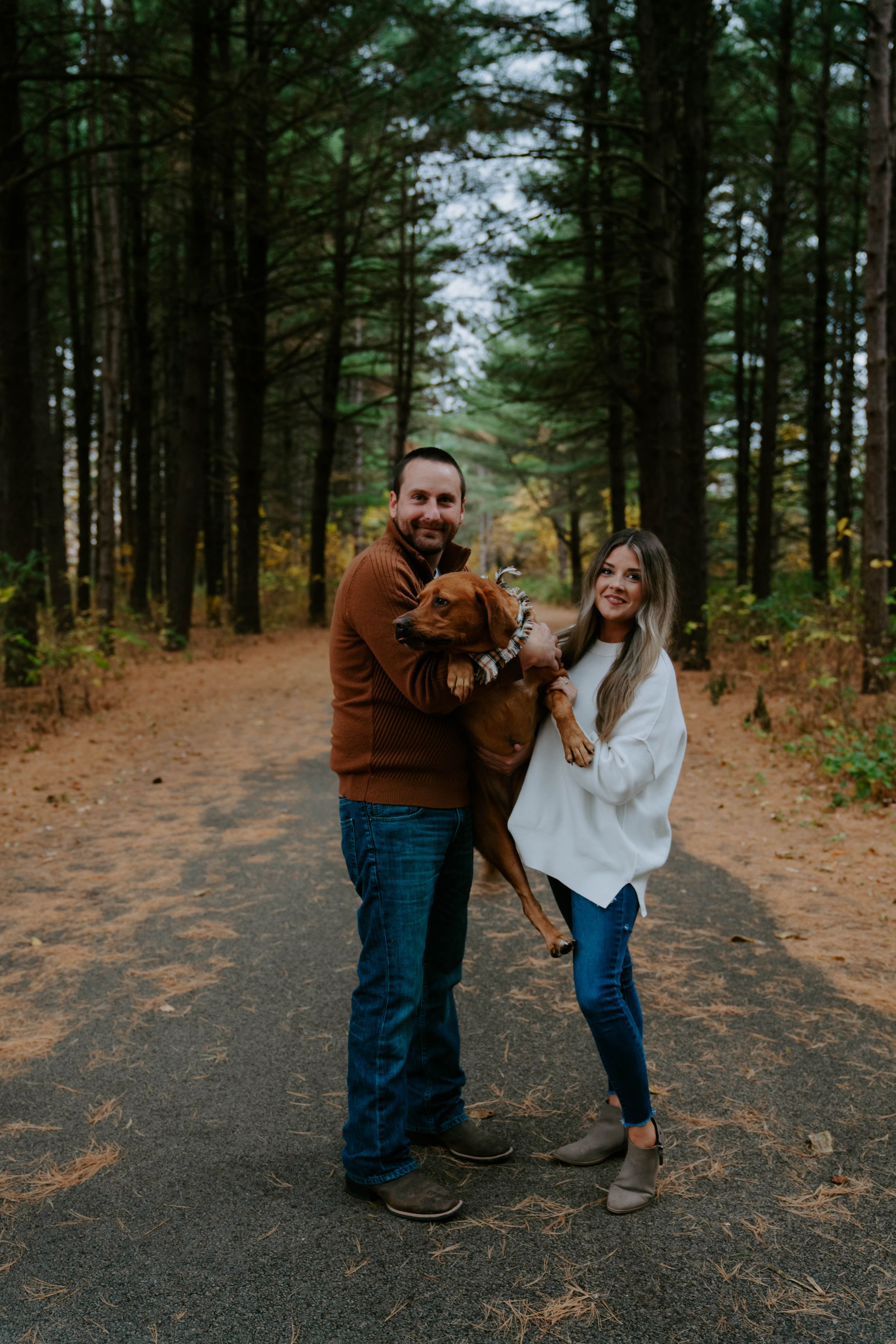 A couple laughs and dances together on a forest path during an autumn photo session.