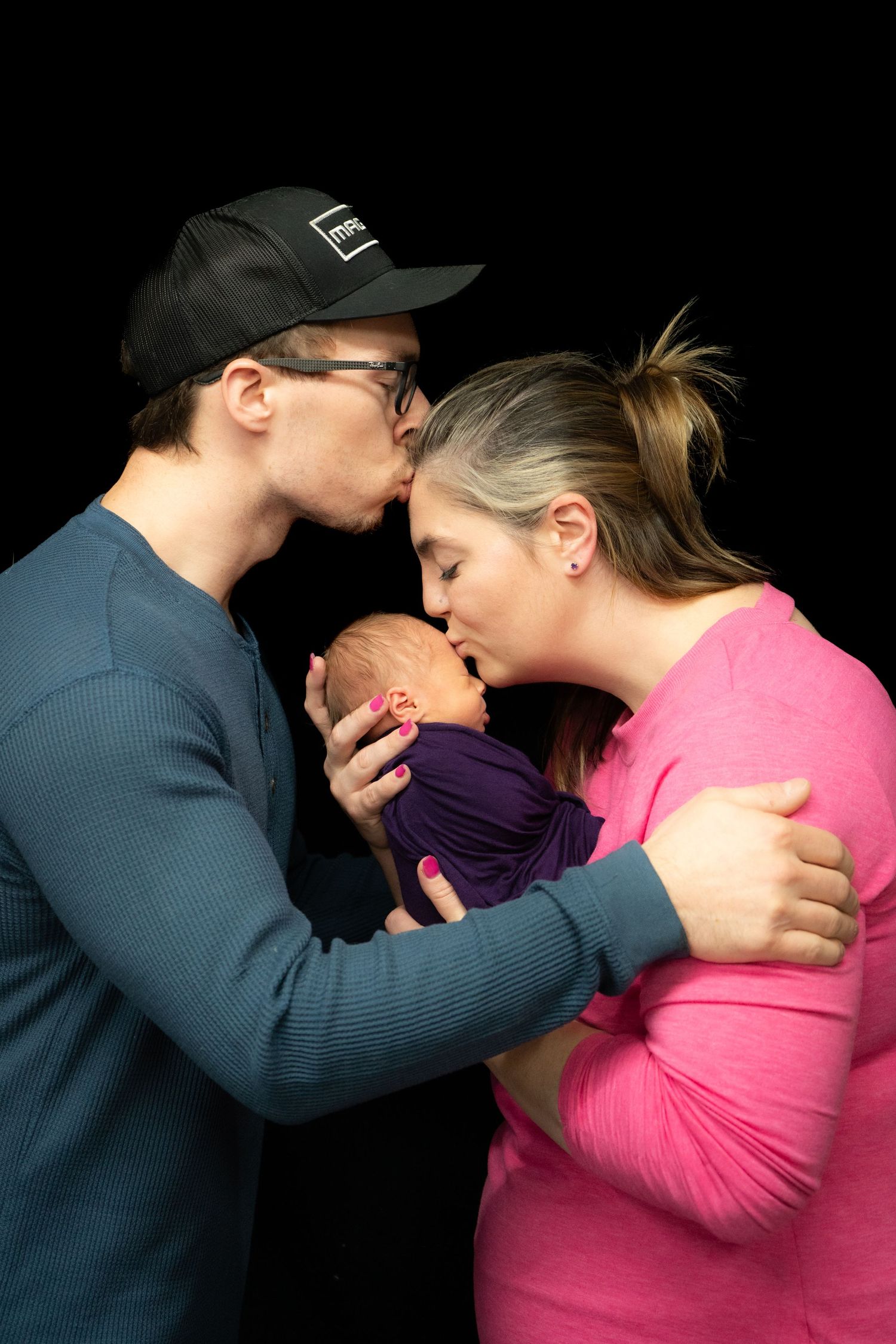 Intimate newborn portrait against black background in dramatic lighting.