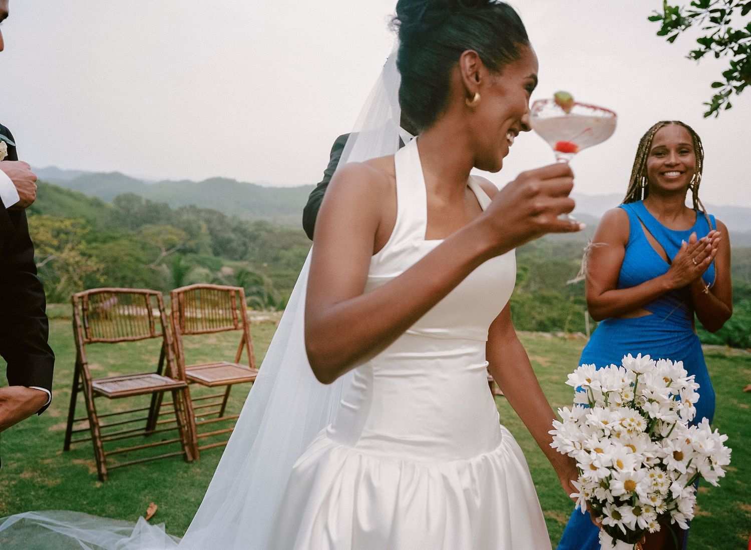 A joyful scene shows a bride laughing during an outdoor wedding ceremony with rolling hills in the background.