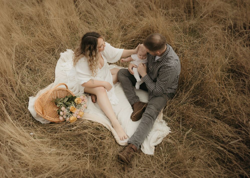 Romantic wedding couple sits intimately in tall brown grass field during golden hour photography session.