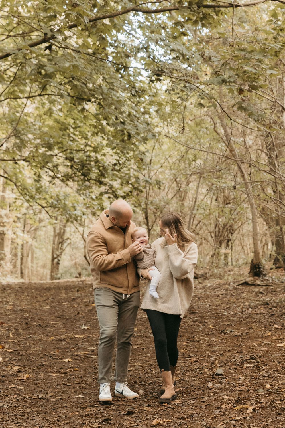 Two people share a sweet moment while walking together on a leaf-covered forest path on an autumn day.