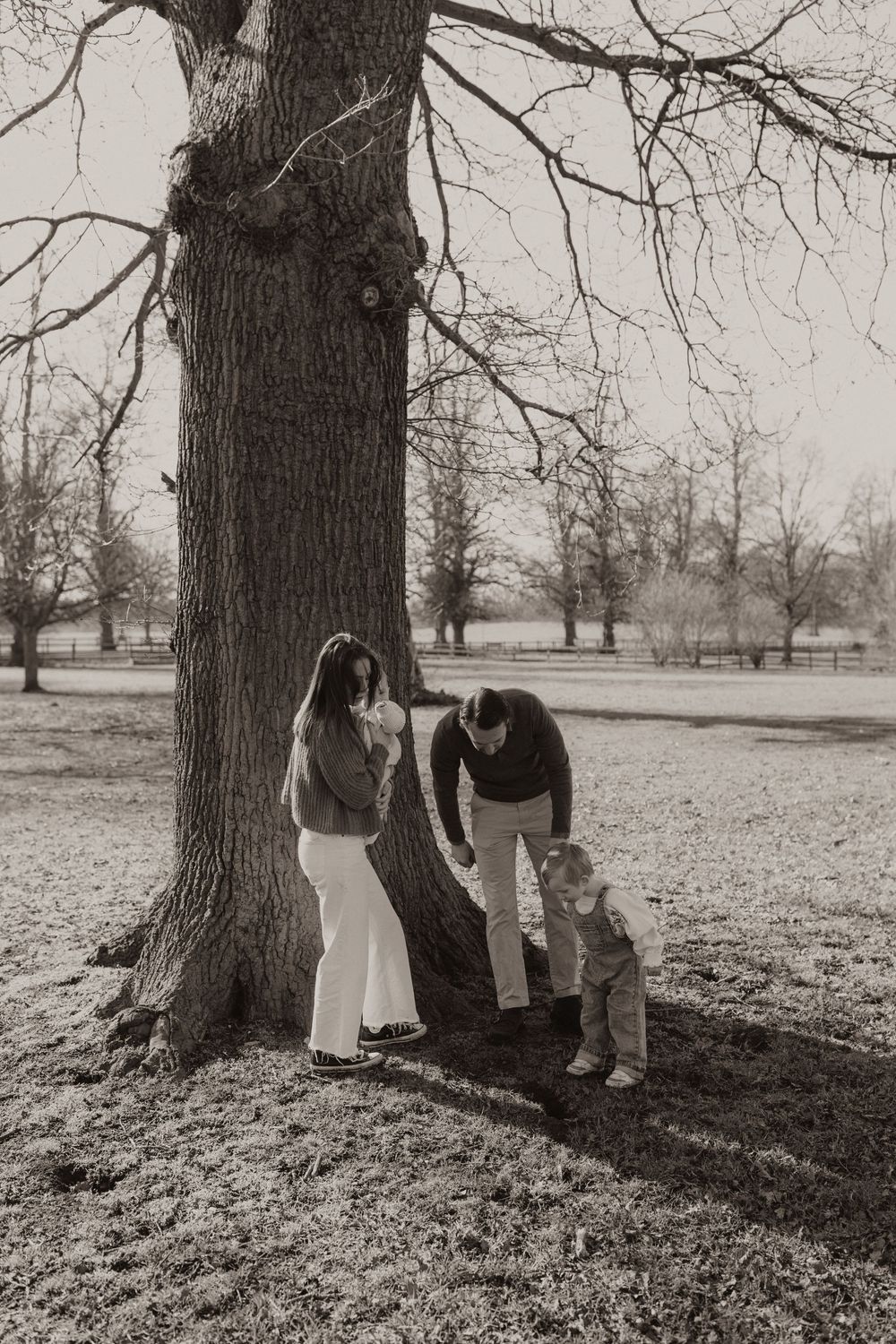 Black and white photo of family gathered around large tree trunk in park setting during autumn.