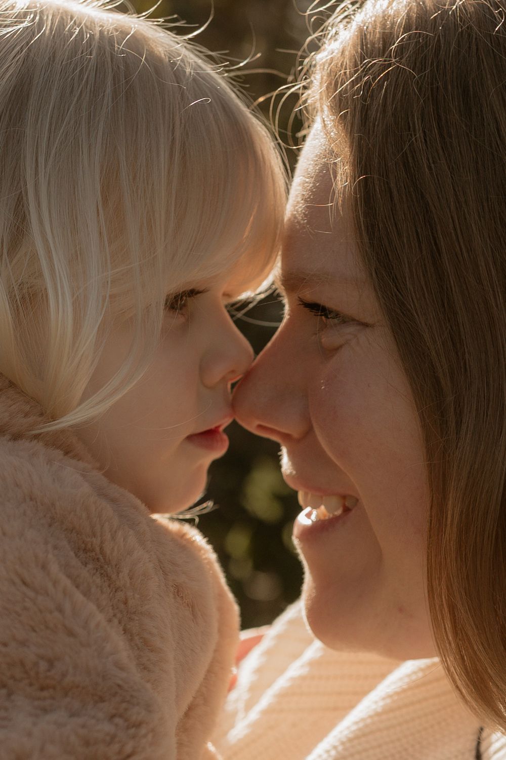 Close up tender moment between a caregiver and young child in warm sunlit setting.