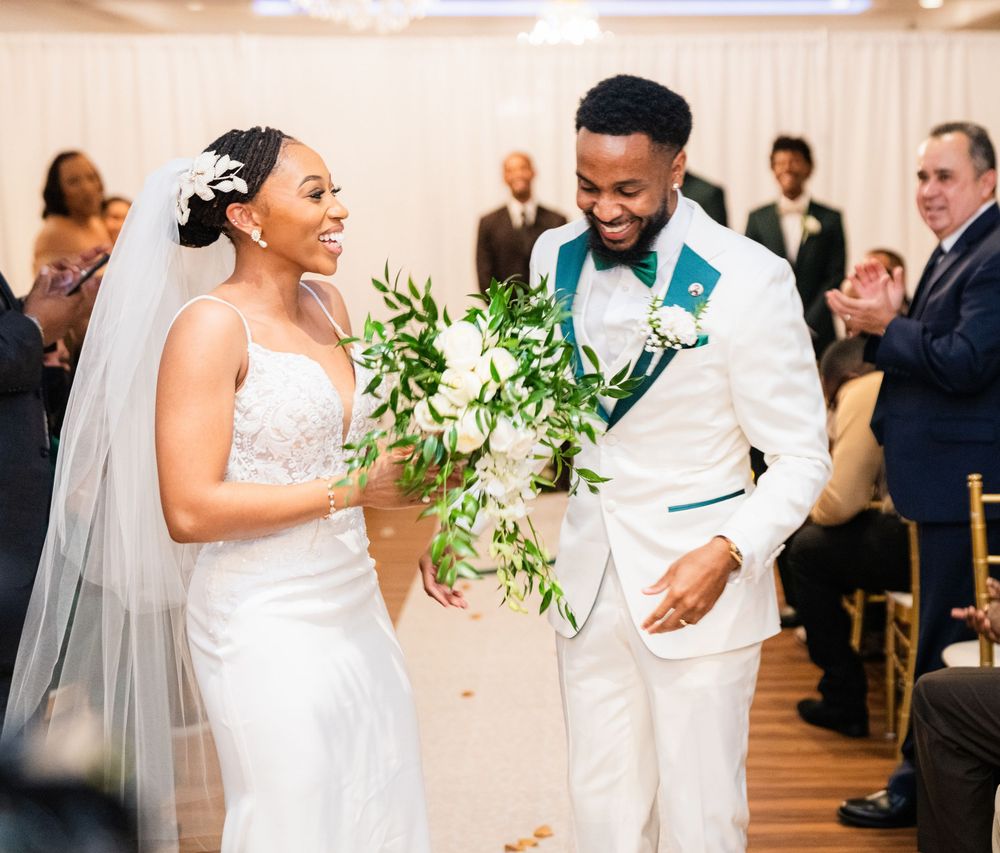 A couple shares a joyful moment during their wedding celebration in an elegant white venue decorated with greenery.