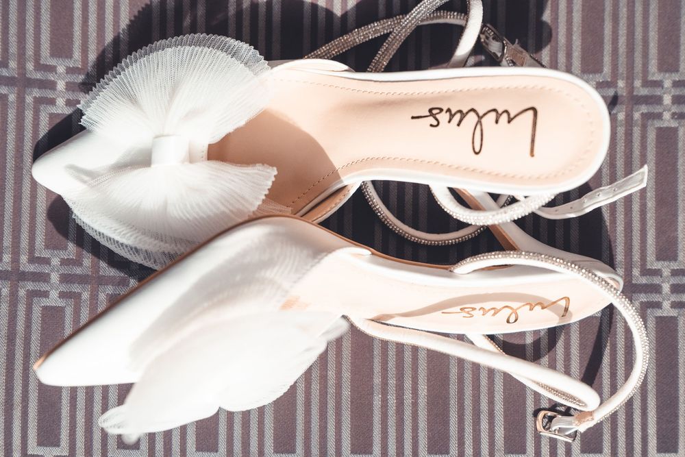 A pair of elegant white pointed-toe slingback heels with a blush pink lining and delicate ankle straps.
