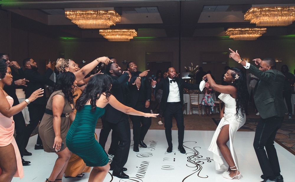 Dancers in formal attire move energetically on a dance floor under ornate crystal chandeliers at an elegant event.