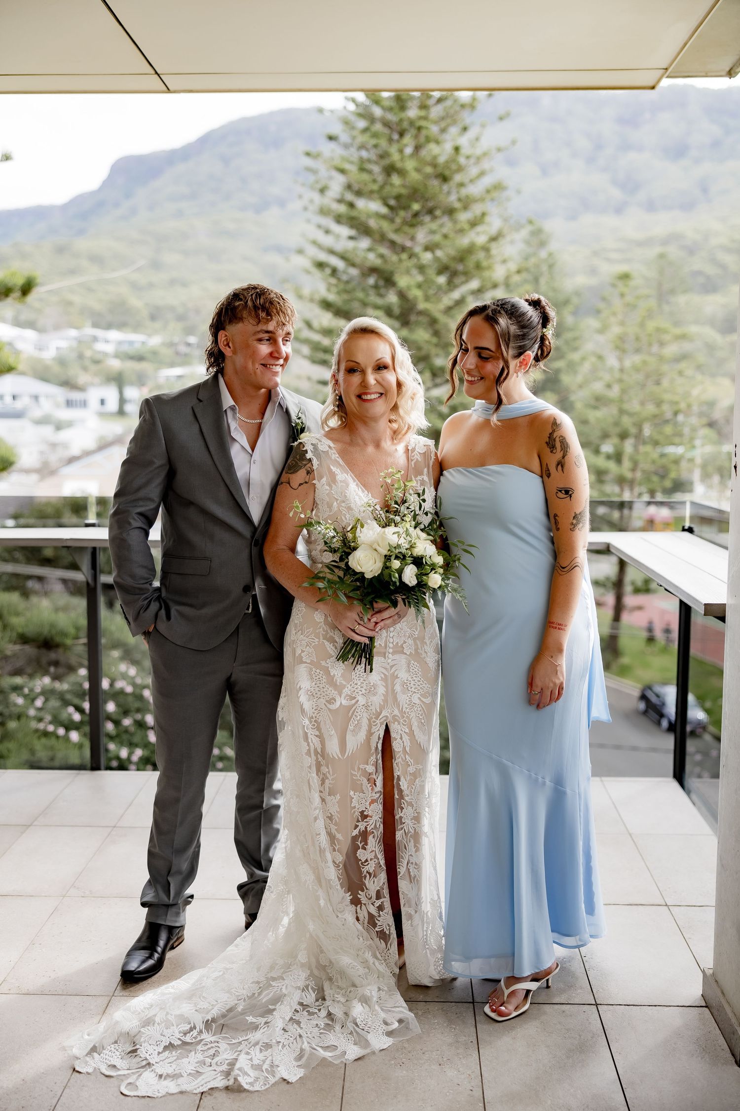 Wedding party poses on balcony with mountains in background wearing formal attire with bride in lace gown.