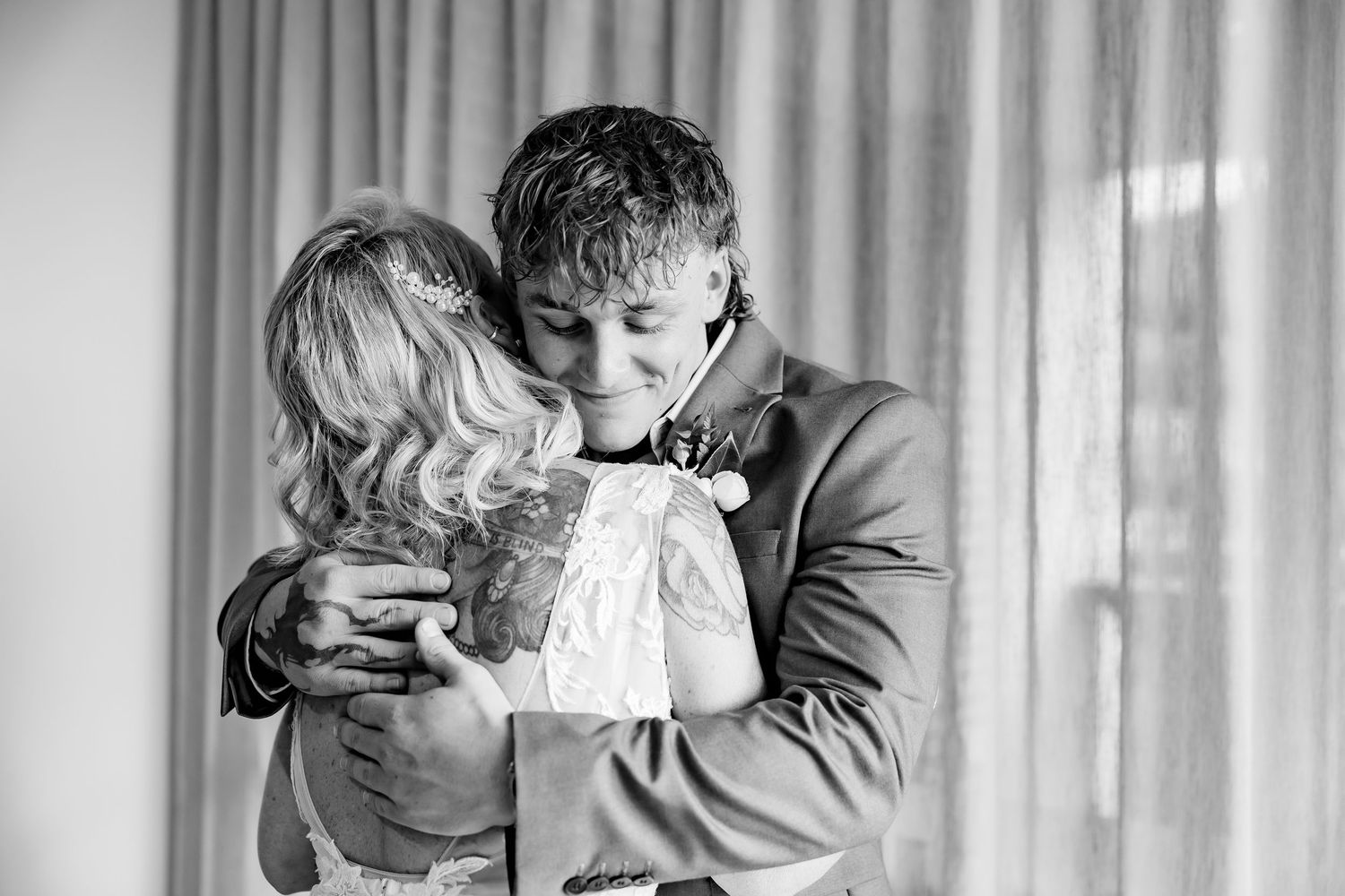 A heartwarming black and white moment of two people sharing an embrace in front of sheer curtains.