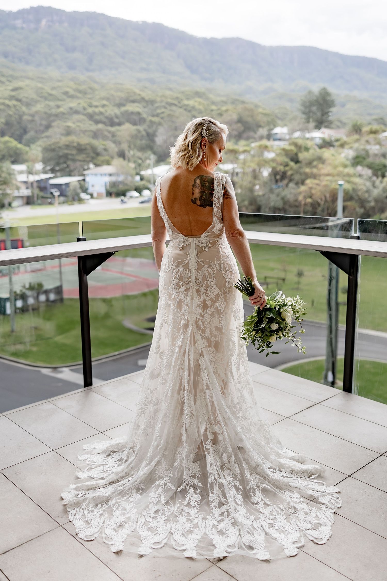 White lace wedding dress with a flowing train displayed on an outdoor balcony with mountain views.