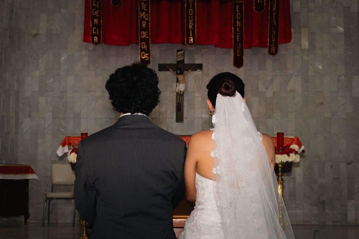 Bride and groom standing at the altar during a church wedding ceremony with a cross above them.