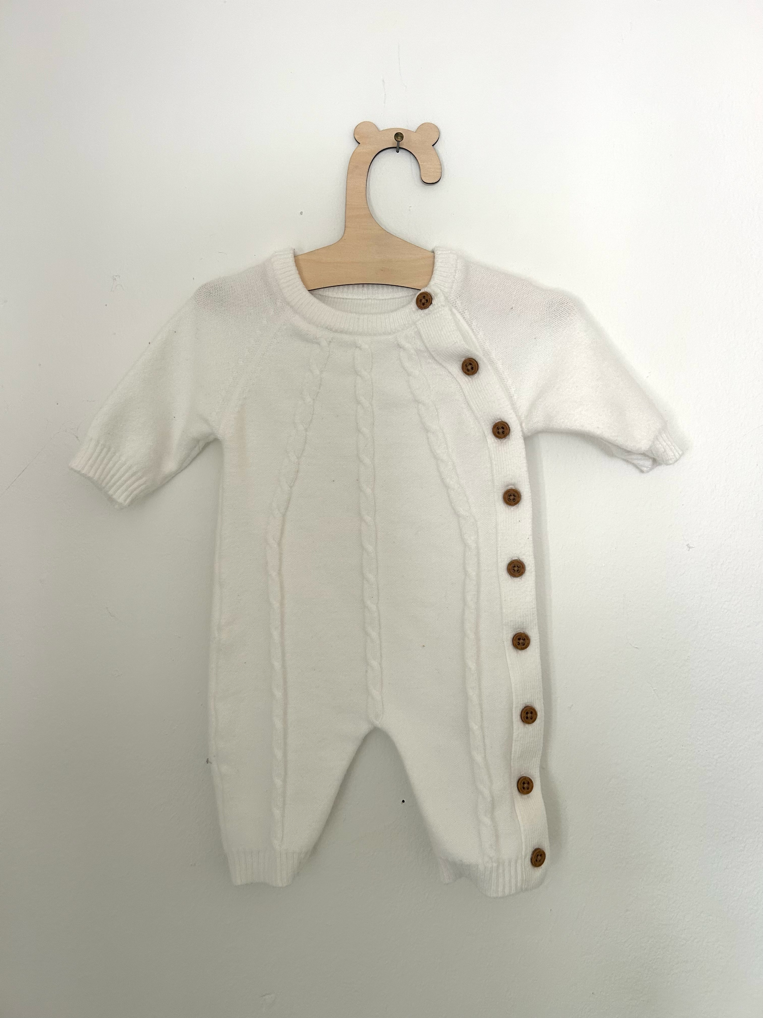 White knit baby romper with 'ONE' text and small bow detail in pink embroidery against hanging clothing background.