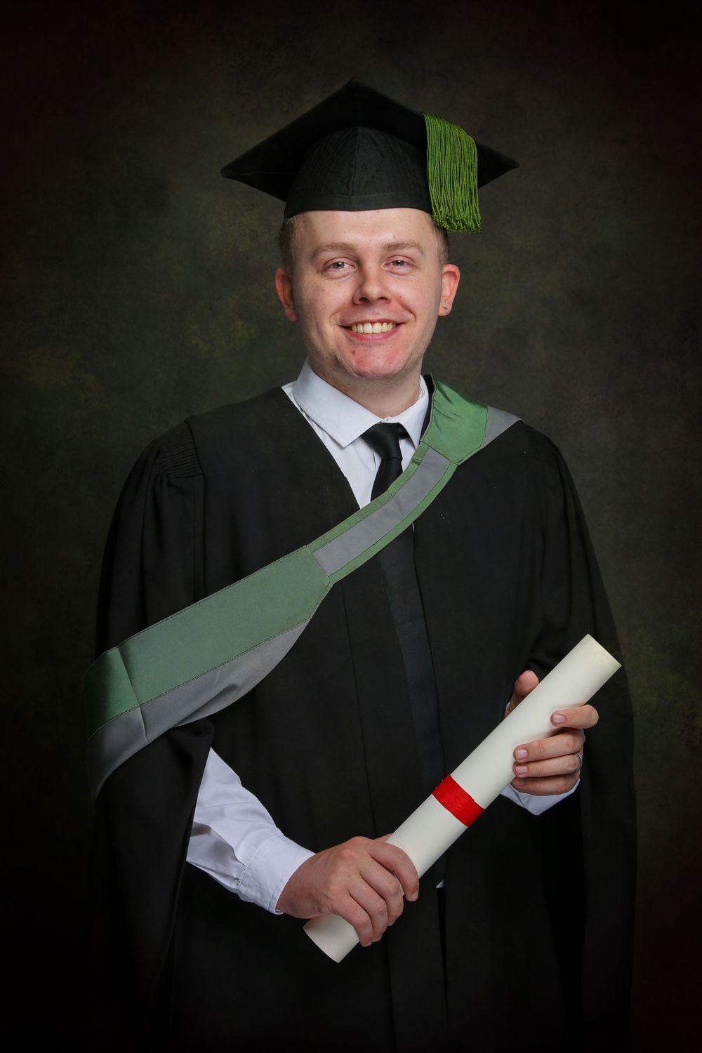 Graduate wearing traditional black cap and gown holds diploma while posing for professional graduation portraits.
