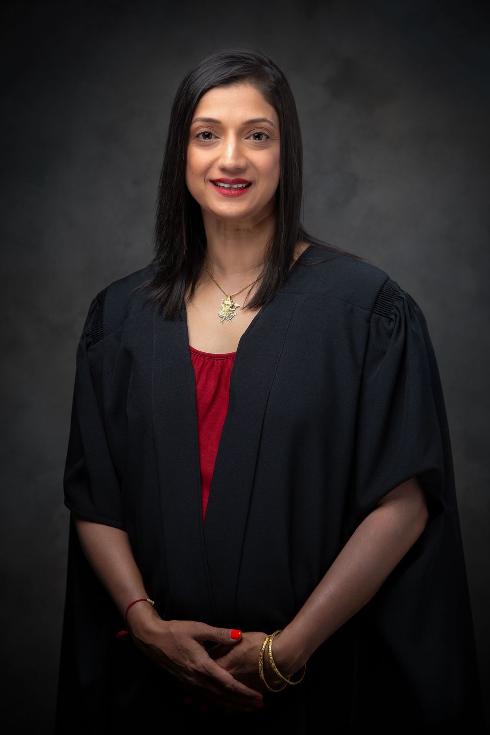 Professional graduation portrait of a graduate in black academic regalia and red top against dark background.