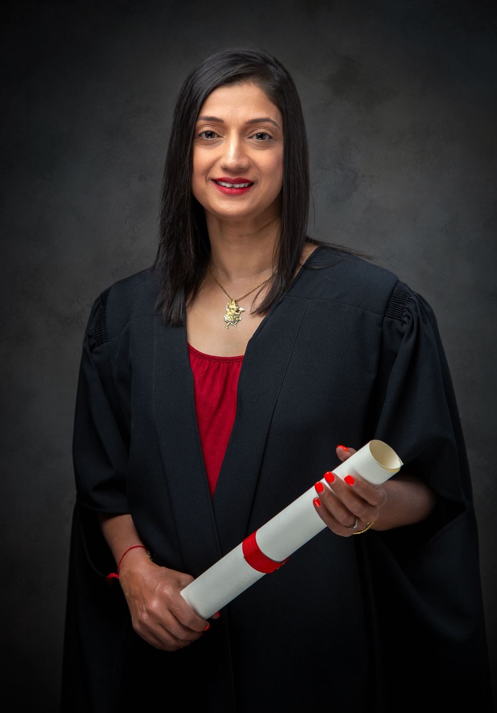 Professional graduation photo of a graduate in academic regalia wearing a black gown and red top while holding a diploma.