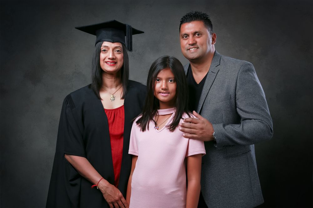 A group of graduates and family members pose together for professional portraits against a dark gray backdrop.
