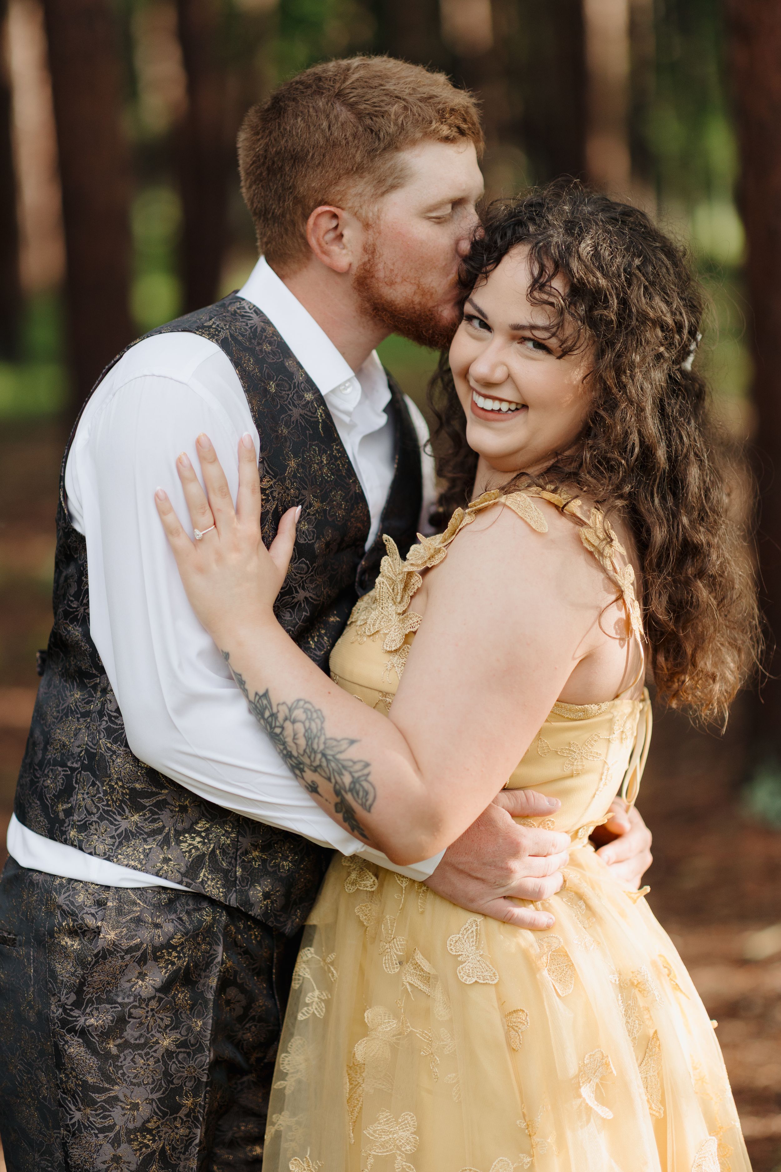 A romantic moment captured between a couple, she in a yellow gown and he in formal wear with a decorative vest.