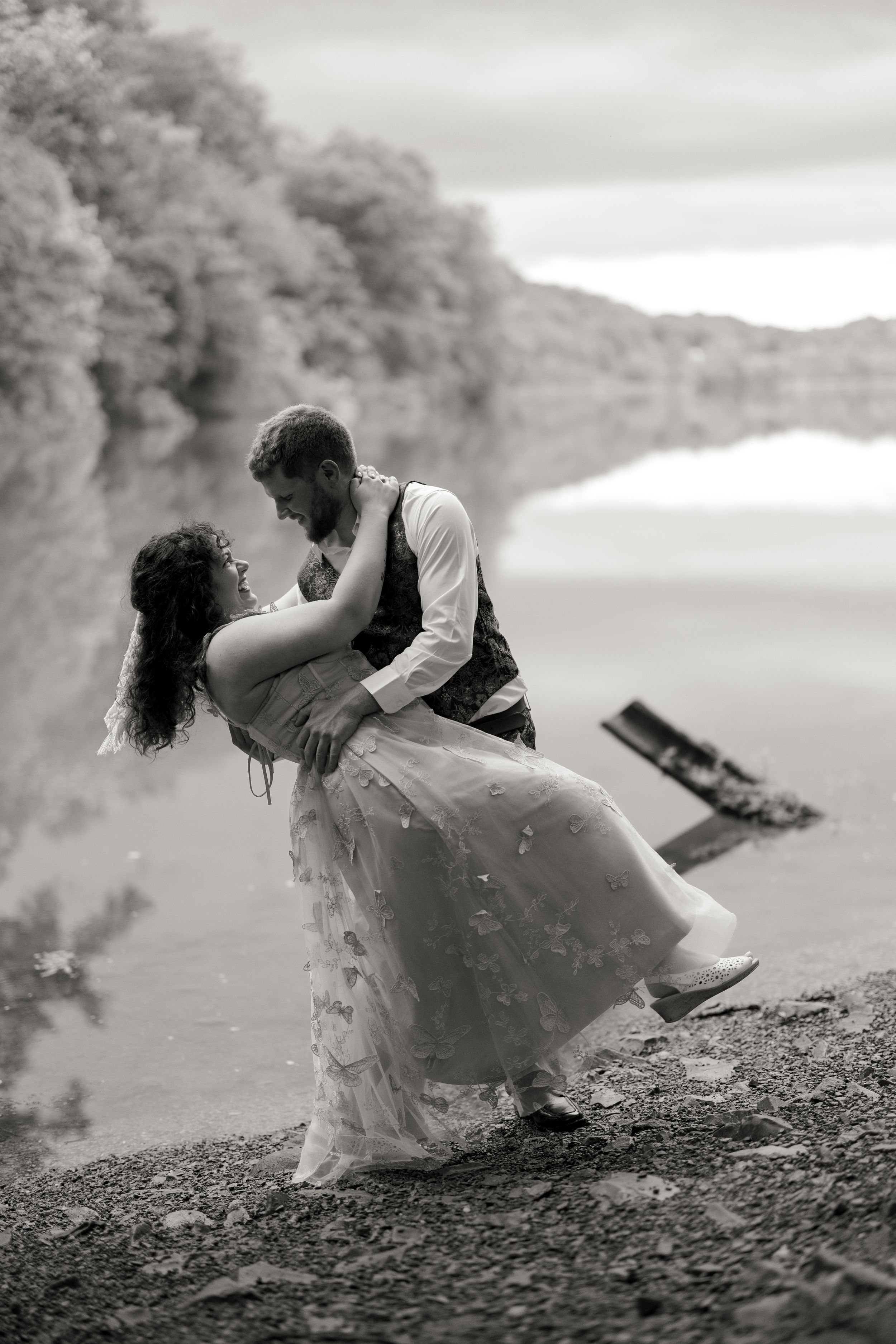 A dramatic black and white photo captures a romantic dip pose by a lake with misty scenery.
