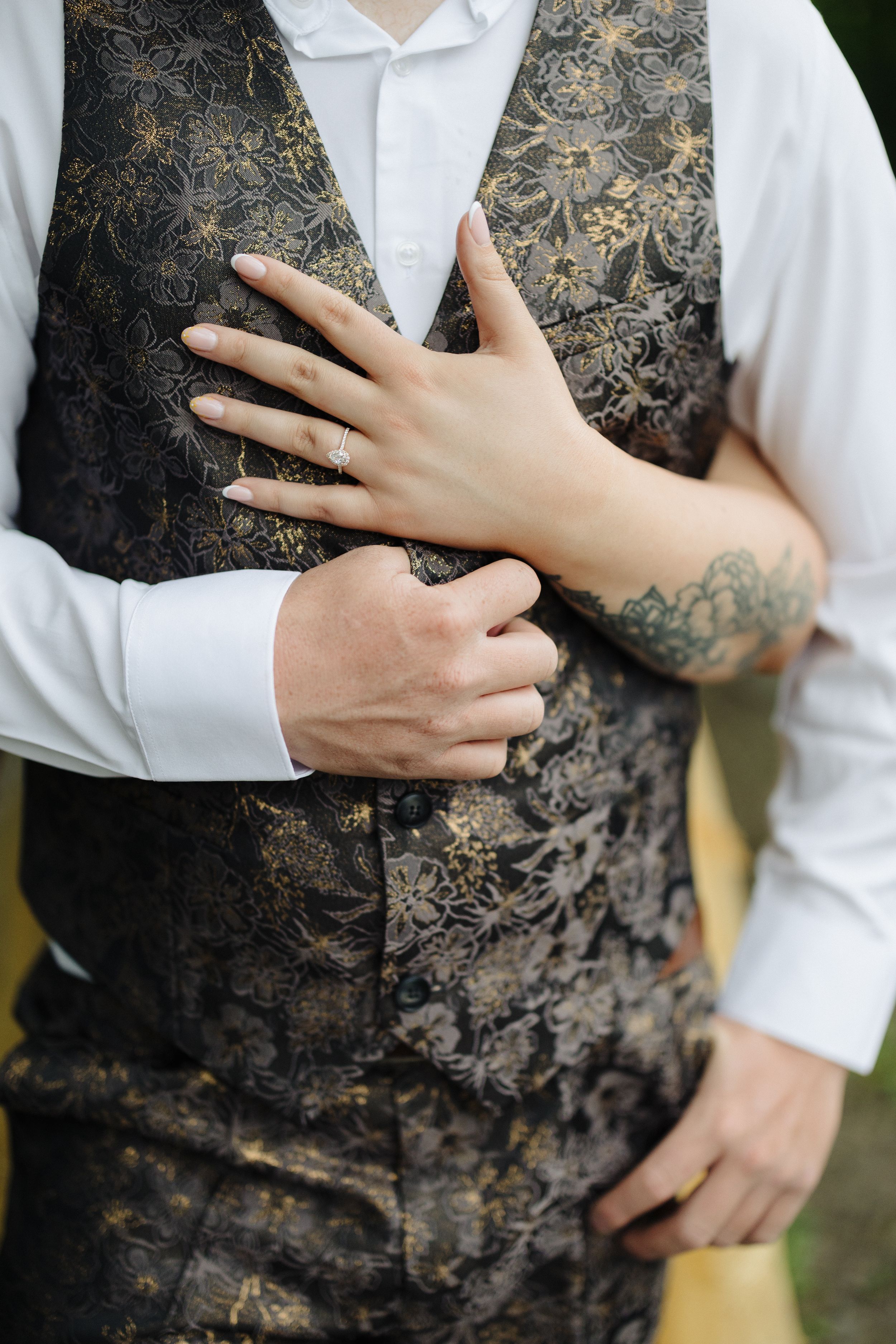 Close-up series showing hands resting against a black and gold floral brocade vest worn with white dress shirt.