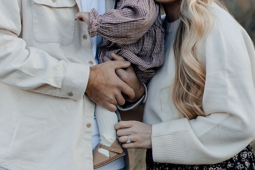 Close up of parents holding small child wearing gingham dress in outdoor setting.