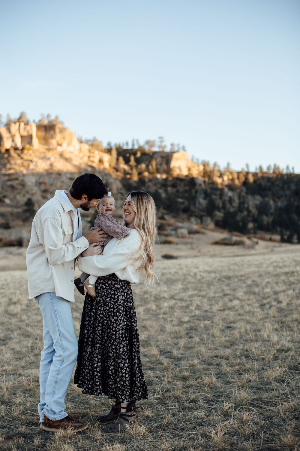 Family shares intimate moment together in field with rocky cliffs at sunset.