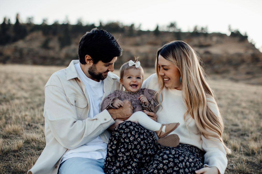 Family sits together on grassy hillside sharing joyful moment at sunset.