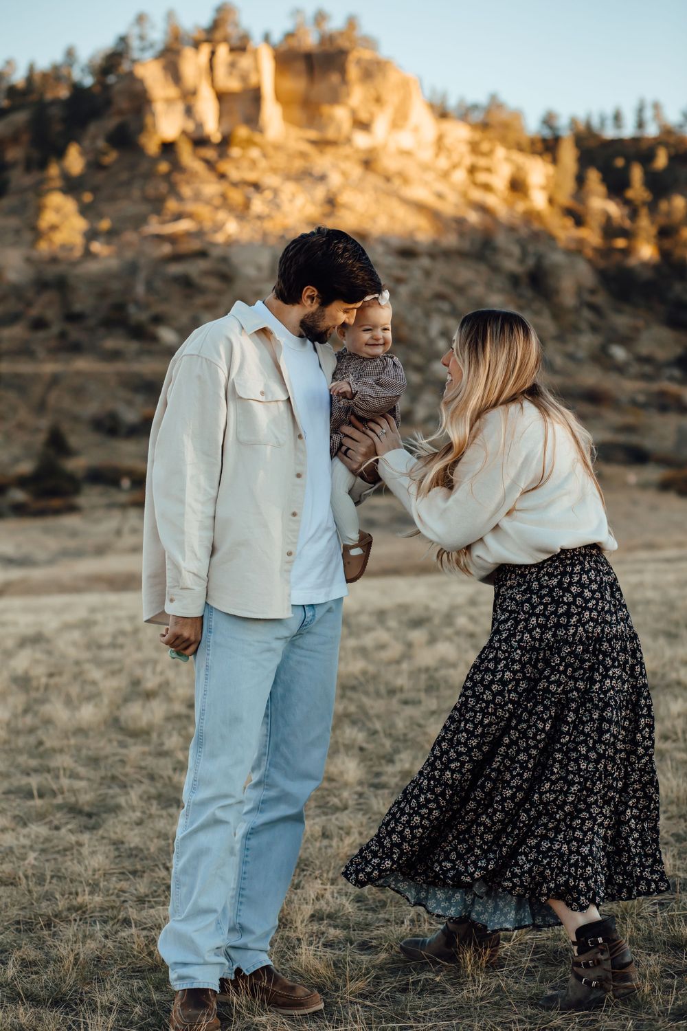 A family shares a tender moment together against a backdrop of rocky cliffs at sunset.