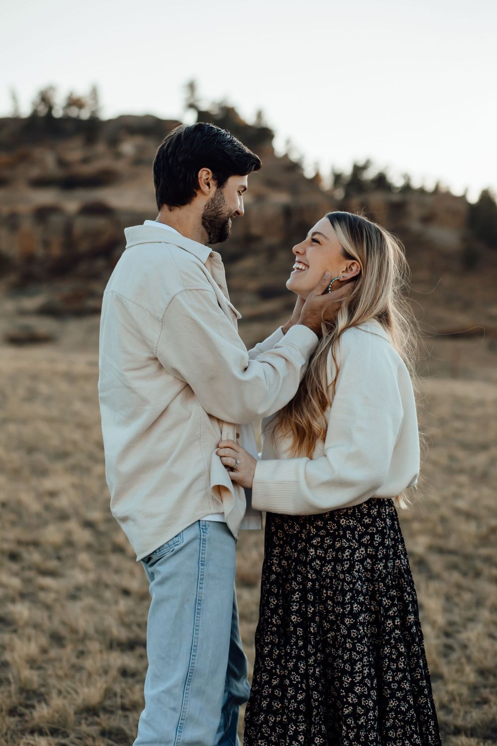 A couple shares an intimate moment while standing in a field with mountains behind them.