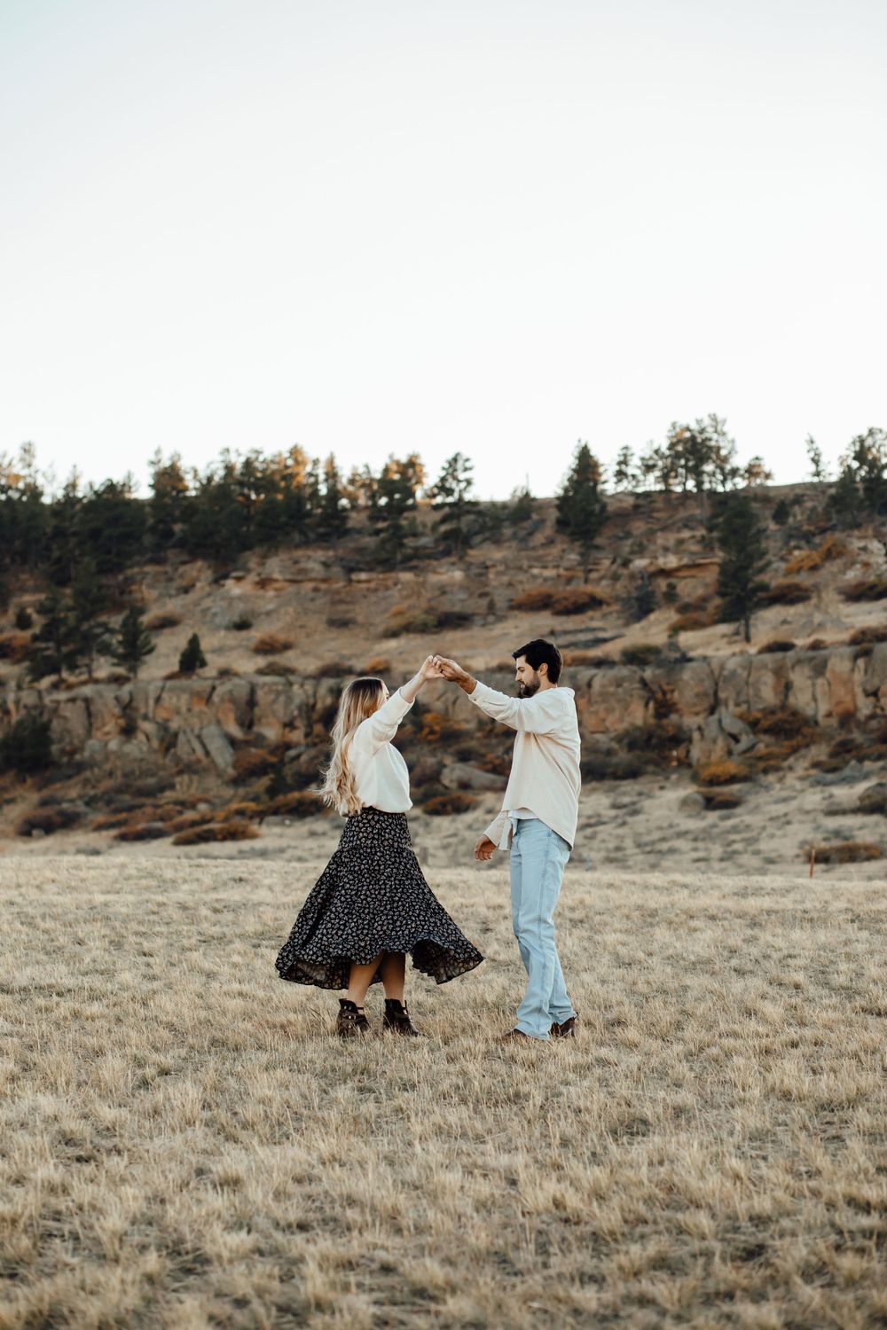 A couple dances together in a field with rocky cliffs in the background.