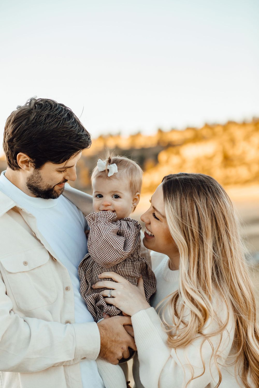 A family shares a tender moment together outdoors during golden hour wearing cream colored outfits.