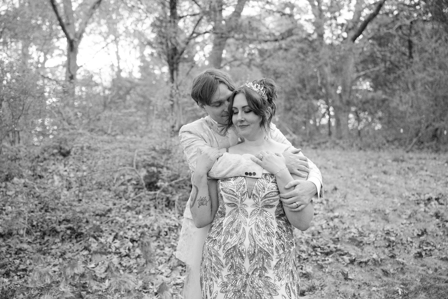 Black and white photo of couple embracing in autumn woodland setting.