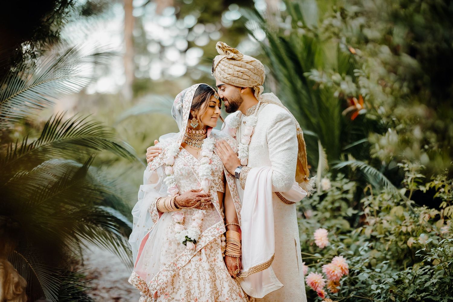 Traditional Indian wedding couple shares intimate moment amidst lush tropical garden setting.