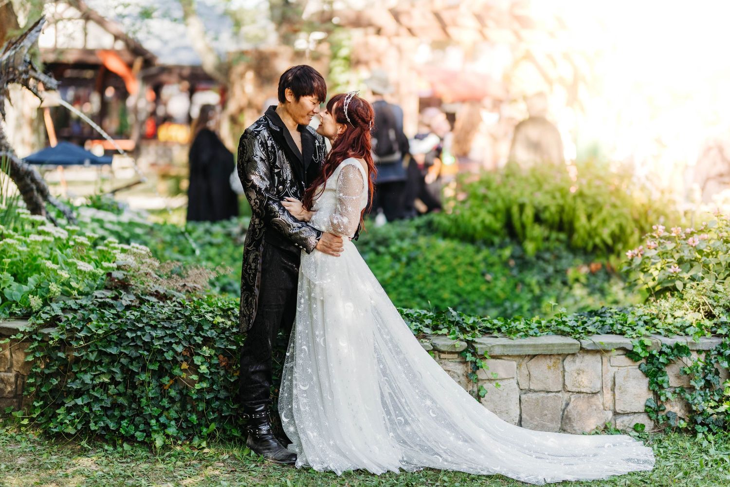 Bride and groom share romantic kiss in sunlit garden at Renaissance-themed outdoor wedding.