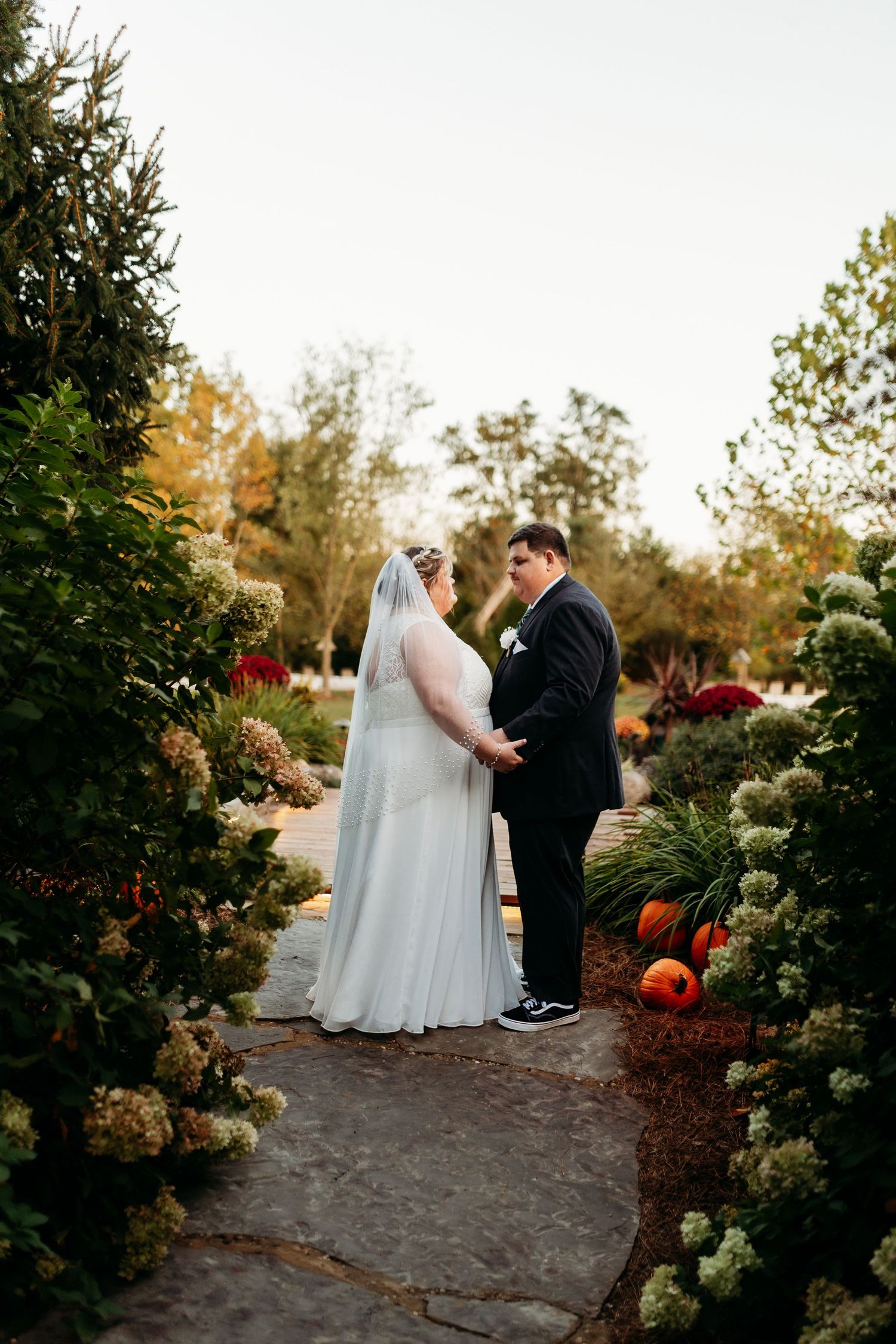 Bride and groom share intimate first look moment in autumn garden with pumpkins and flowers.